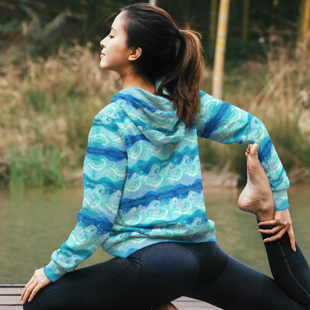 A cozy unisex Aqua Storm Waves Beach Hoodie by Chameleon Surf, featuring a vibrant aqua storm waves design. This sustainable hoodie is made from 95% recycled polyester and 5% spandex, offering a soft cotton-feel fabric on the outside and a brushed fleece interior for extra warmth. The relaxed fit and double-lined hood with drawstrings make it perfect for beach bonfires, lounging at home, or any chilly evening. Embrace comfort, style, and eco-friendly fashion with this stylish beach hoodie.